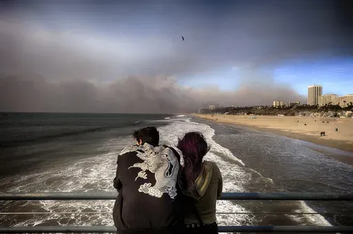 Visitors to the Santa Monica pier look out at smoke from a wildfire in the Pacific Palisades blows over the beach in Santa Monica, Calif., on Wednesday, Jan. 8, 2025. (AP Photo/Richard Vogel)