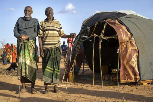 Mohamed Kheir Issack, 80, right, and and Issack Farow Hassan, 75, stand outside Issack's shelter at a camp for displaced people on the outskirts of Dollow, Somalia on Tuesday, Sept. 20, 2022. The two blind men are friends and as close as brothers, gripping each other's hands in their mutual darkness as tightly as they hold their canes. Near the end of their lives, the most alarming drought in more than half a century in Somalia has stripped them of their animals and homes. (AP Photo/Jerome Delay