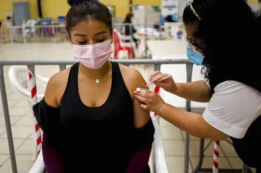 A healthcare worker administers an AstraZeneca booster shot for COVID 19 at a vaccination center in Guatemala City, Tuesday, March 1, 2022.  (AP Photo/Moises Castillo)