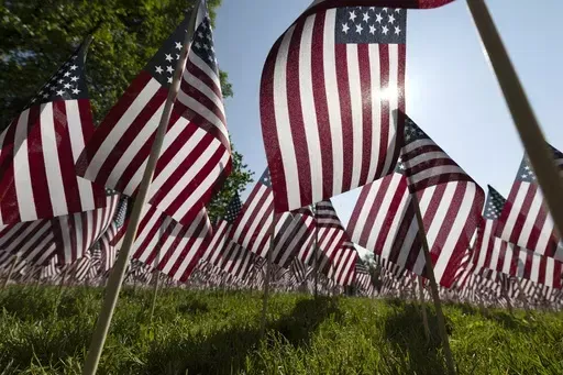 The sun shines through the flags in the Memorial Day Flag Garden on Boston Common, May 27, 2023, in Boston. Memorial Day is supposed to be about mourning the nation’s fallen service members. But it’s come to anchor the unofficial start of summer and retail discounts. (AP Photo/Michael Dwyer, file)