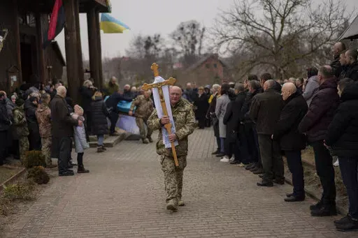 People attend a funeral ceremony for Ukrainian military servicemen Roman Rak and Mykola Mykytiuk in Starychi, western Ukraine, Wednesday, March 16, 2022. Rak and Mykytiu were killed during Sunday's Russian missile strike on a military training base in Yavoriv. (AP Photo/Bernat Armangue)