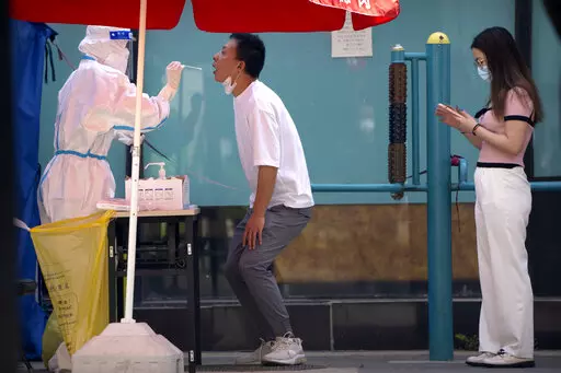 A worker wearing a protective suit swabs a man's throat for a COVID-19 test at a testing site during the second consecutive day of mass testing in Beijing, Wednesday, May 4, 2022. Beijing on Wednesday closed around 10% of the stations in its vast subway system as an additional measure against the spread of coronavirus. (AP Photo/Mark Schiefelbein)
