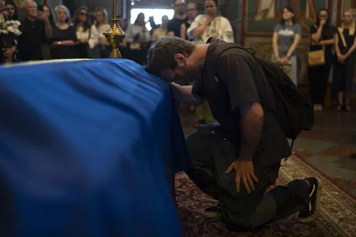 A mourner kneels while paying his final respects for Ukrainian writer Victoria Amelina during a memorial service for Amelina in Kyiv, Ukraine, Tuesday, July 4, 2023. The award-winning writer was killed in June by a Russian missile attack on a popular restaurant frequented by journalists and aid workers in eastern Ukraine. (AP Photo/Jae C. Hong)