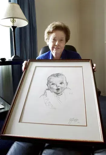 Ann Taylor Cook, poses at her Tampa, Fla., home Wednesday afternoon Feb. 4, 2004, with a copy of her photo that is used on all Gerber baby food products. Ann Turner Cook, whose cherubic baby face was known the world over as the original Gerber baby, has died. She was 95. Gerber announced Cook's passing in an Instagram post on Friday, June 3, 2022. (AP Photo/Chris O'Meara, File)